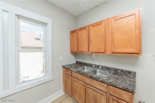 kitchen with dark stone counters, light wood-style floors, baseboards, and a sink