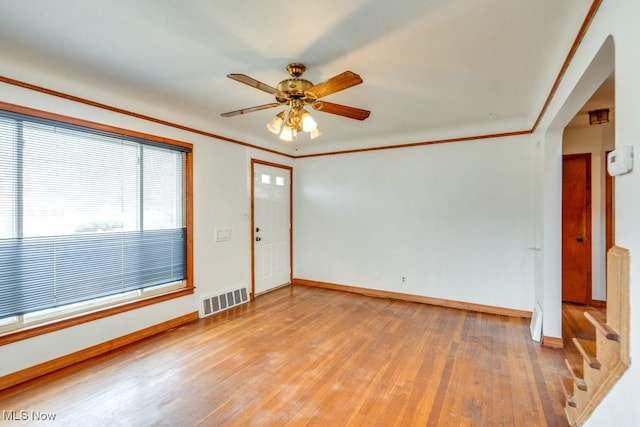 unfurnished room with ceiling fan, visible vents, light wood-style flooring, and ornamental molding