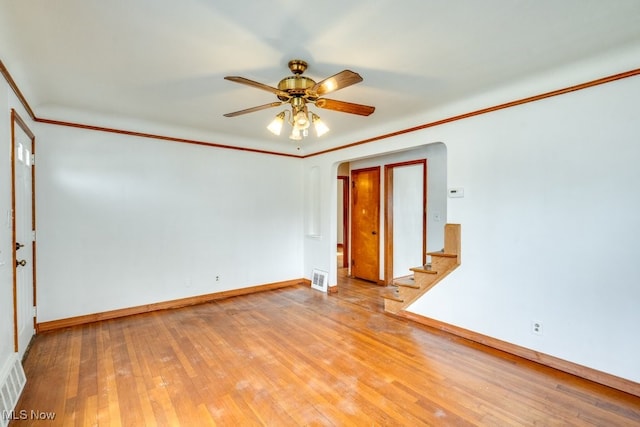 empty room featuring a ceiling fan, baseboards, light wood finished floors, arched walkways, and crown molding