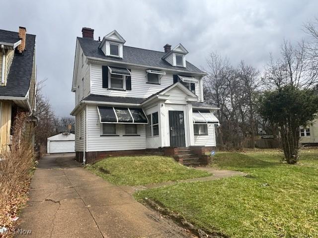 view of front facade featuring a chimney, a front yard, a detached garage, and an outdoor structure