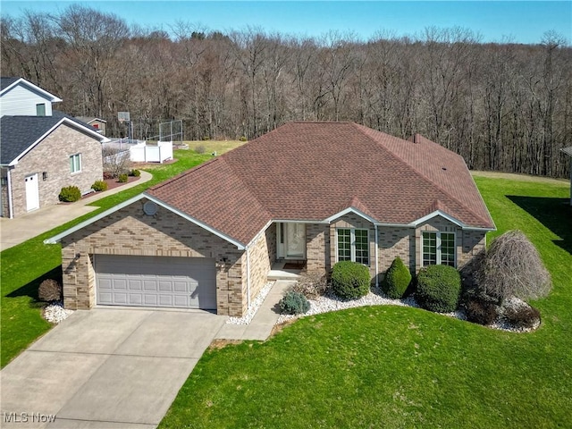 single story home with a front yard, a forest view, a garage, and driveway