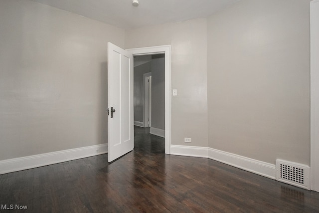 empty room featuring dark wood finished floors, visible vents, and baseboards