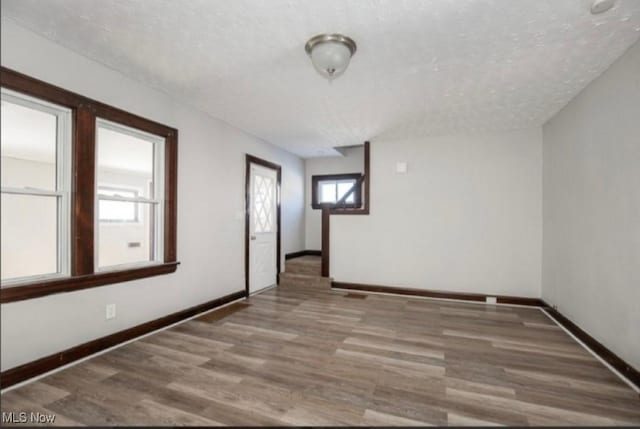 unfurnished room with a textured ceiling, baseboards, and wood finished floors