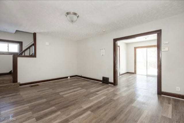 unfurnished room with stairway, baseboards, a textured ceiling, and wood finished floors