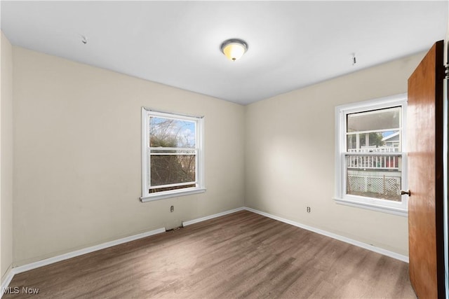empty room with wood finished floors, a healthy amount of sunlight, and baseboards