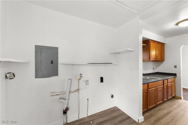 laundry area with electric panel, cabinet space, wood finished floors, and a sink