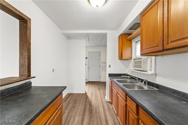 kitchen with a sink, brown cabinets, dark countertops, and wood finished floors