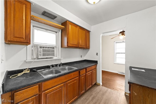 kitchen with visible vents, brown cabinets, a sink, dark countertops, and light wood-style floors