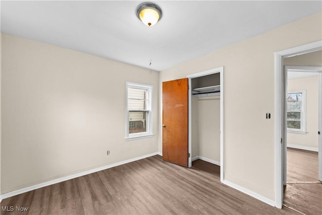 unfurnished bedroom with a closet, multiple windows, baseboards, and wood finished floors