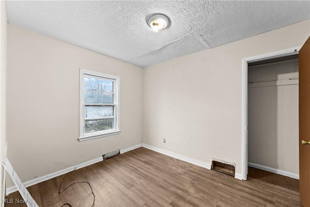 unfurnished bedroom featuring a closet, baseboards, a textured ceiling, and wood finished floors