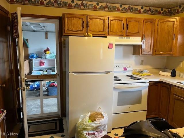 kitchen featuring light countertops, under cabinet range hood, brown cabinets, and white appliances