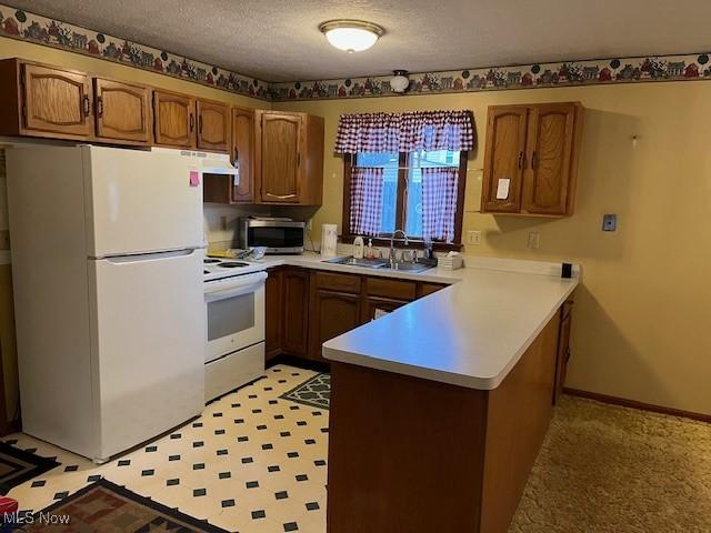 kitchen with light countertops, white appliances, a textured ceiling, a sink, and a peninsula