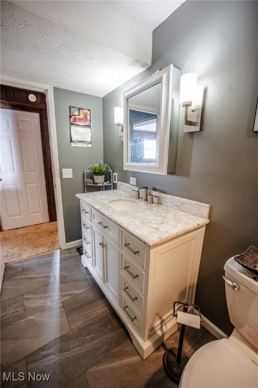 bathroom with toilet, a textured ceiling, vanity, and baseboards