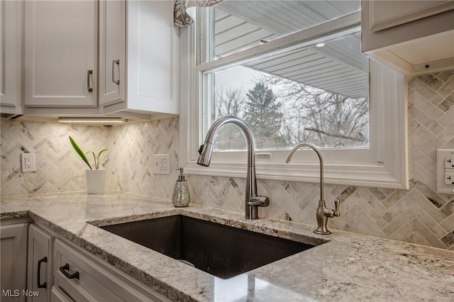 kitchen featuring light stone countertops, a sink, white cabinets, and a wealth of natural light