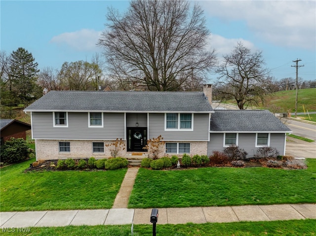 bi-level home with a chimney, a front yard, and brick siding