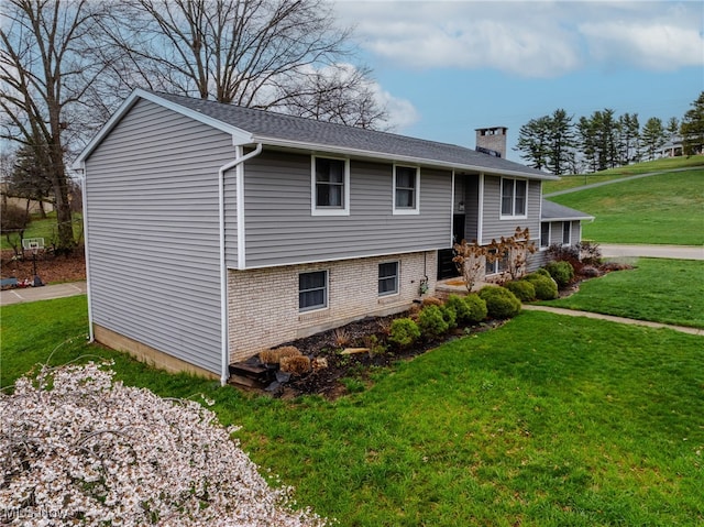 split foyer home with roof with shingles, brick siding, a chimney, and a front lawn