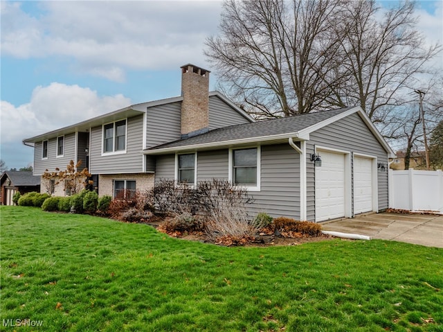 rear view of property featuring a yard, a garage, a chimney, fence, and driveway