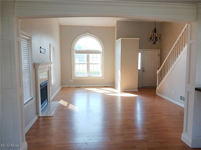 unfurnished living room featuring baseboards, wood finished floors, visible vents, and a chandelier