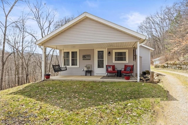 bungalow-style home featuring a front lawn, covered porch, and dirt driveway
