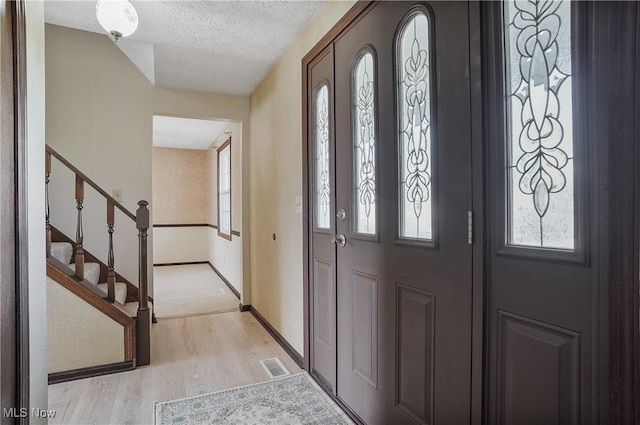 foyer entrance featuring baseboards, visible vents, stairs, light wood-style floors, and a textured ceiling