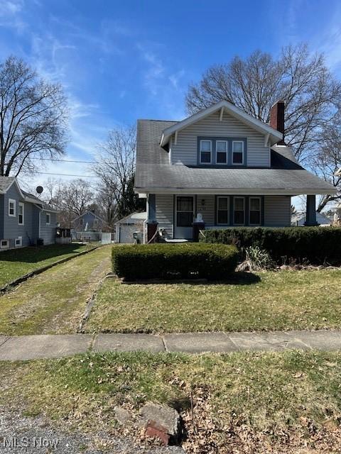 view of front of home with a shingled roof, a front yard, a garage, and a chimney