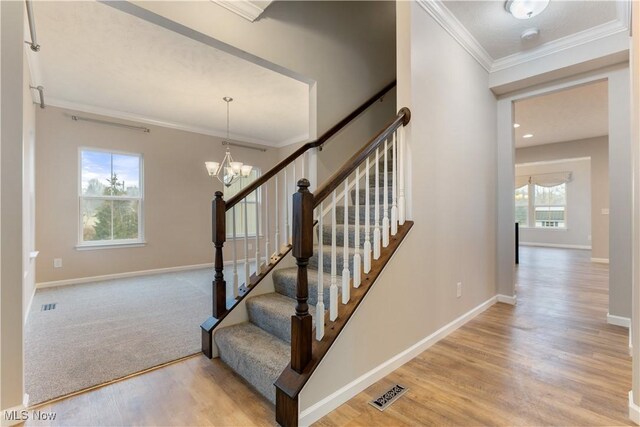 staircase featuring visible vents, baseboards, ornamental molding, wood finished floors, and a notable chandelier