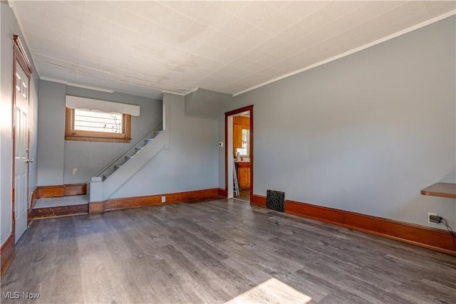 unfurnished living room featuring baseboards, wood finished floors, stairs, and crown molding