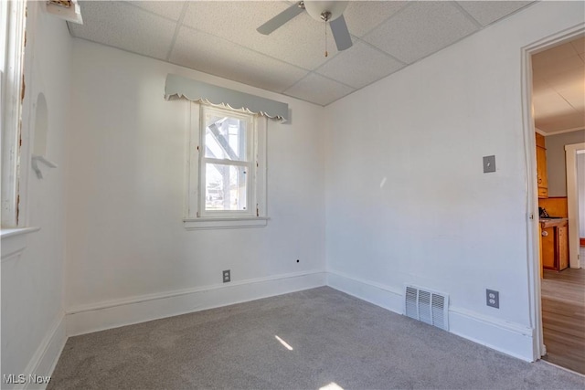 carpeted spare room with a ceiling fan, visible vents, a drop ceiling, and baseboards