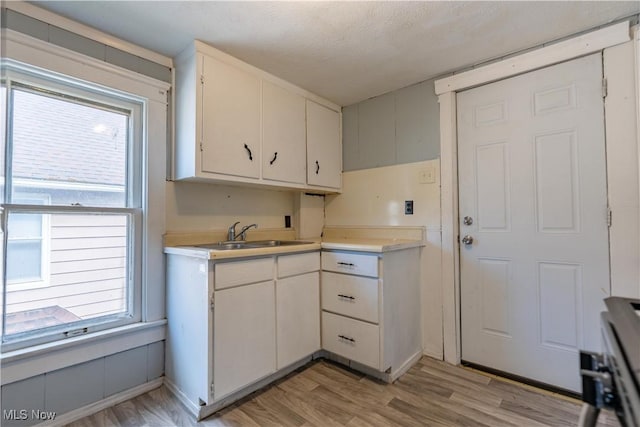 kitchen with light wood-style flooring, white cabinetry, light countertops, and a sink