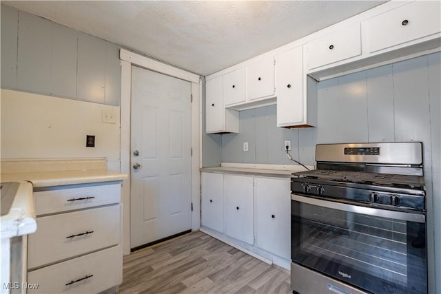 kitchen featuring light wood finished floors, a textured ceiling, stainless steel gas range, and light countertops