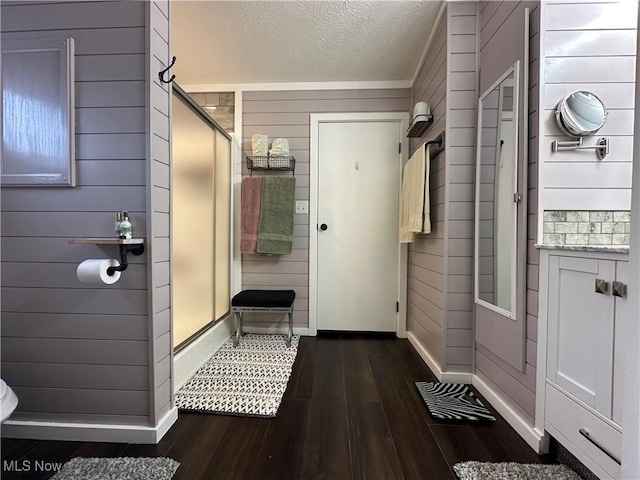 bathroom featuring wood finished floors, baseboards, a shower stall, wood walls, and a textured ceiling