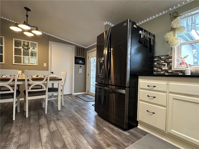 kitchen featuring dark countertops, vaulted ceiling, decorative backsplash, black refrigerator with ice dispenser, and dark wood-style flooring