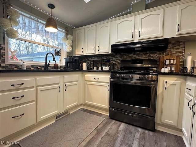 kitchen featuring under cabinet range hood, dark wood finished floors, tasteful backsplash, and stainless steel gas stove