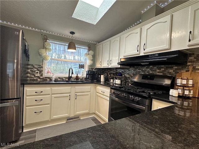 kitchen with under cabinet range hood, a sink, tasteful backsplash, stainless steel appliances, and a skylight
