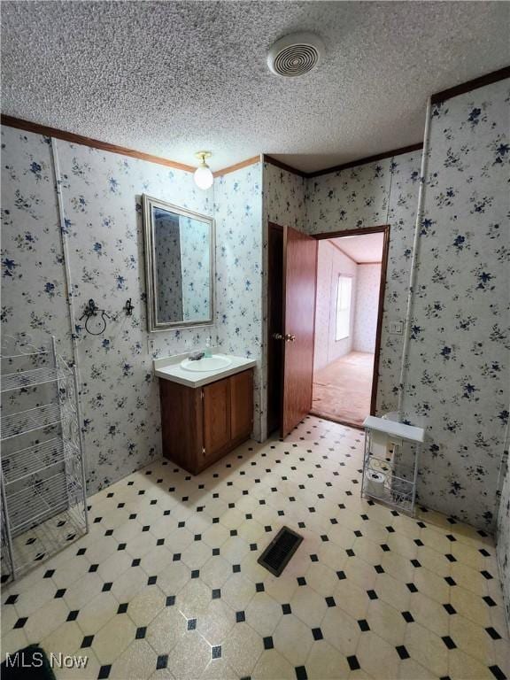 bathroom featuring a textured ceiling, crown molding, and wallpapered walls