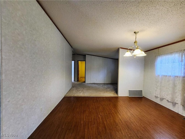 unfurnished room featuring a notable chandelier, visible vents, a textured ceiling, and wood finished floors