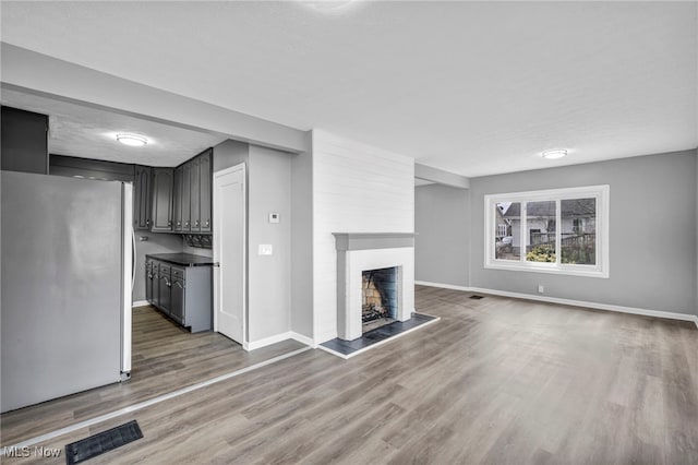 unfurnished living room featuring baseboards, visible vents, a large fireplace, and wood finished floors