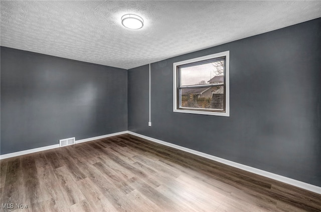 spare room with wood finished floors, a textured ceiling, baseboards, and visible vents
