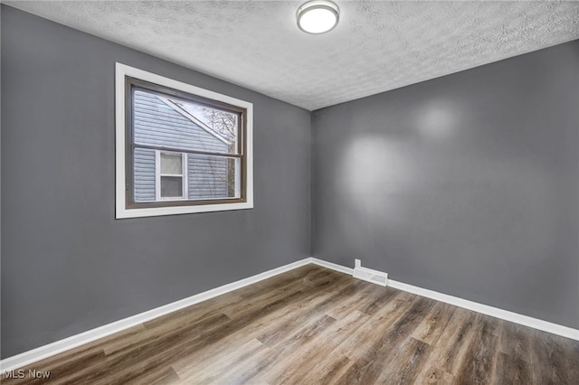 empty room with visible vents, a textured ceiling, baseboards, and wood finished floors