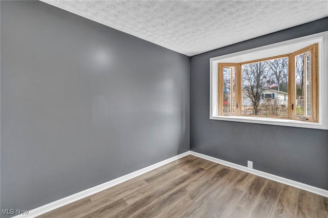 empty room featuring baseboards, a textured ceiling, and wood finished floors
