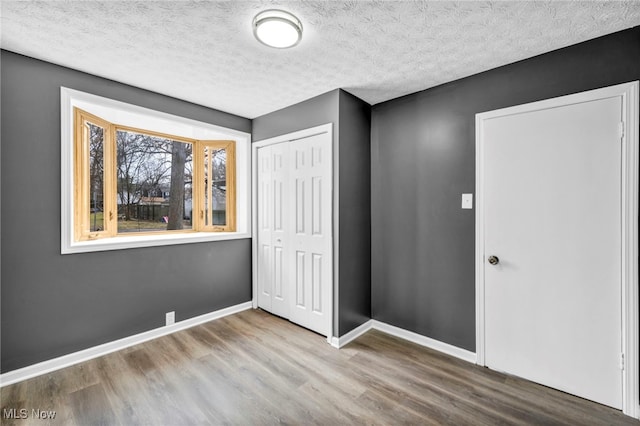 unfurnished bedroom with baseboards, a textured ceiling, wood finished floors, and a closet