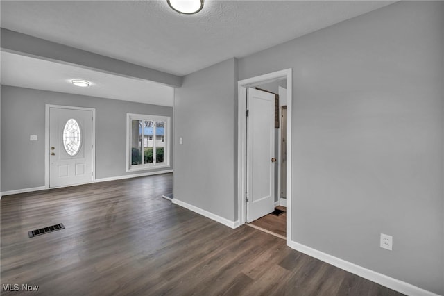 foyer entrance with dark wood-style flooring, a textured ceiling, baseboards, and visible vents