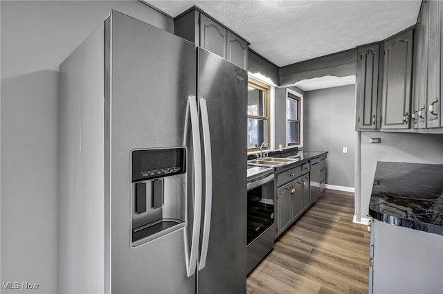 kitchen with dark countertops, a sink, stainless steel appliances, and gray cabinetry
