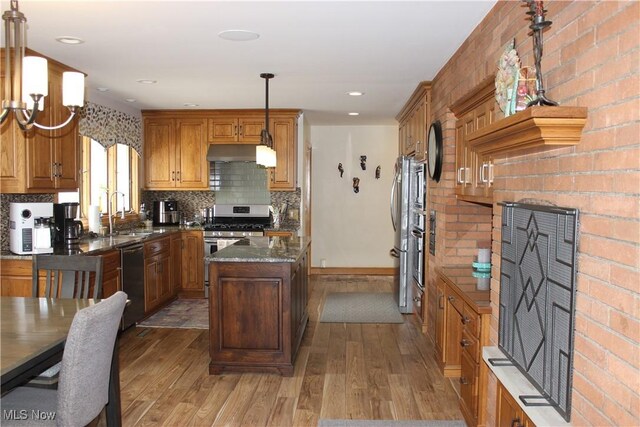 kitchen with wood finished floors, appliances with stainless steel finishes, under cabinet range hood, a sink, and a center island