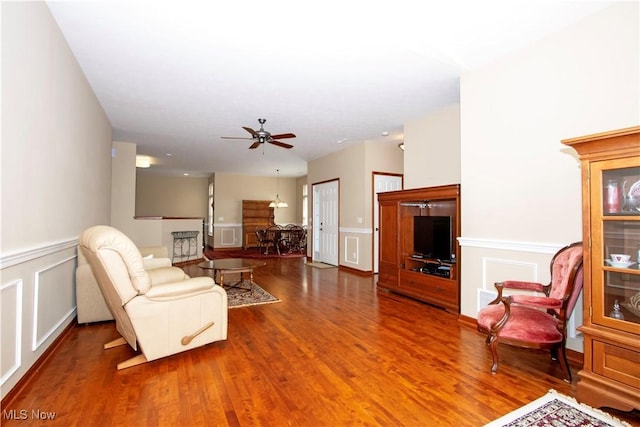 living room featuring a wainscoted wall, wood finished floors, a decorative wall, and a ceiling fan