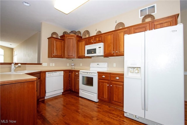 kitchen with a sink, dark wood-style floors, brown cabinetry, white appliances, and visible vents