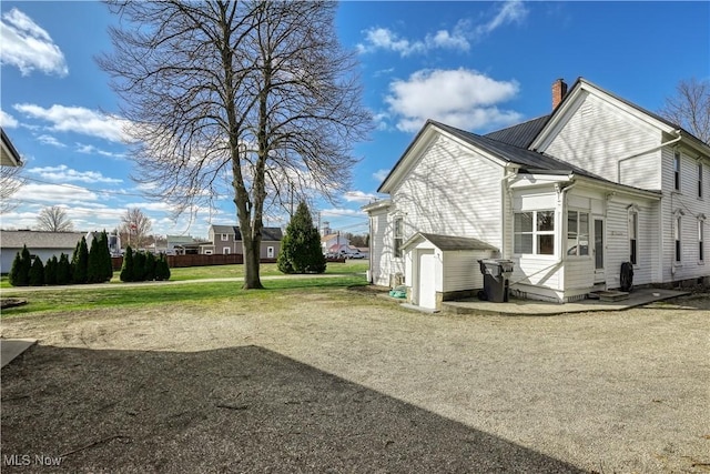 view of property exterior featuring a chimney, an outdoor structure, a storage unit, a yard, and entry steps