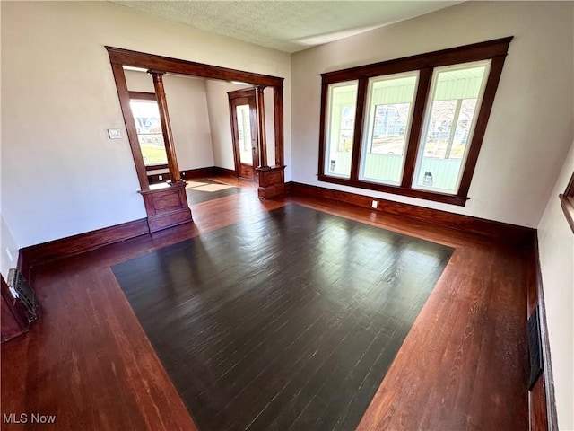 unfurnished living room with ornate columns, baseboards, a textured ceiling, and wood finished floors