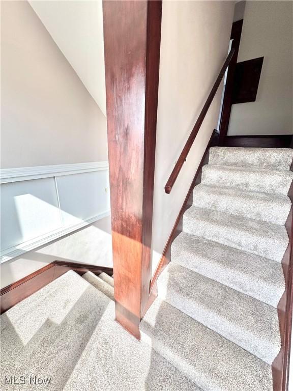 stairway featuring lofted ceiling and wainscoting