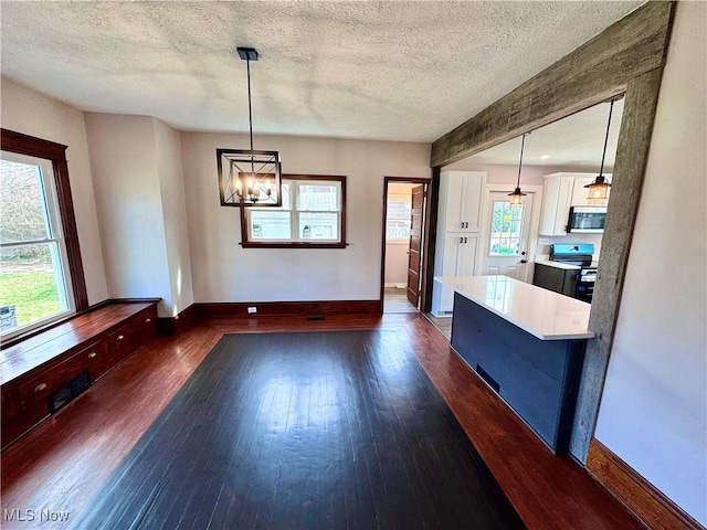 unfurnished dining area with an inviting chandelier, dark wood-style flooring, baseboards, and a textured ceiling